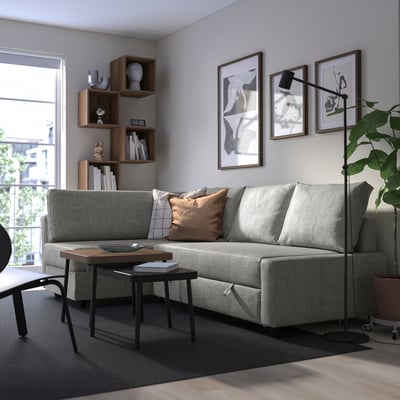 Modern living room with a gray FRIHETEN sectional sofa, large cushions, wooden coffee table, and wall art. Plant and bookshelf.
