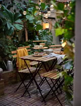 Outdoor dining setup with wooden table, FULLSPÄCKAD bamboo serving tray, string lights, and potted plants.