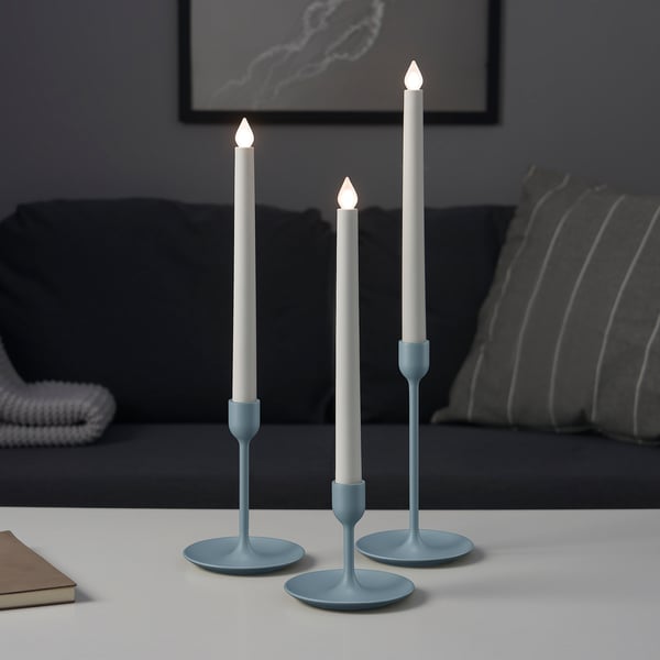 Three lighted candles of varying heights on blue holders, adding cozy ambiance to a living room.