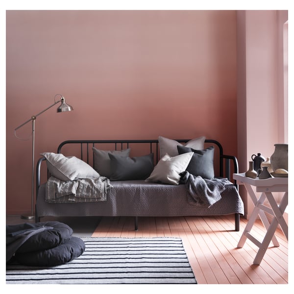 Day-bed FYRESDAL: black metal frame, grey linens, wooden floor, pink walls.