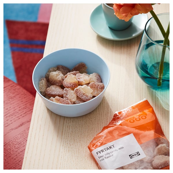 Gummy candies in bowl next to FYRTAKT cola sour jellies and blue vase with flower.