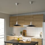 Modern black pendant lamps illuminate kitchen island, highlighting bowl and cutting board.