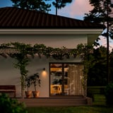 Cozy house patio adorned with GETKÅL white string lights, potted plants, and wooden bench. Lights span above, illuminating the entrance and garden.