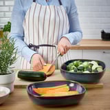 A person prepares vegetables in a kitchen using GLADELIG oven dishes for serving.