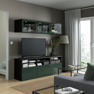 Modern living room with dark olive-green GLASSVIK cabinet, flat-screen tv, grey couch, lamp, and floral arrangement.