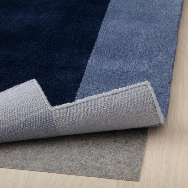 Blue geometric rug folded, showing thick wool texture, laid on wooden floor.