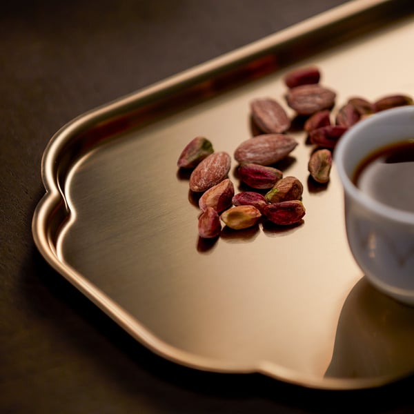 A shiny, gold tray holds scattered pistachio nuts and a small cup of coffee. Elegant and stylish, perfect for serving.