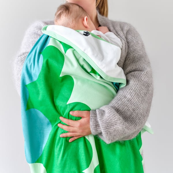 A person holding a baby in a green and white blanket, ideal for nap time, featuring soft cotton material.