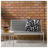 A modern bench sits against a brick wall, featuring a black and white patterned cushion. A small table next to it holds a drink.
