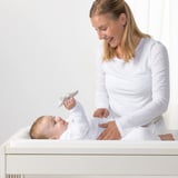Woman in white tends baby on GULLIVER changing table with practical storage.