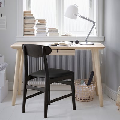 Minimalist desk setup with black chair, white lamp, books, and basket.