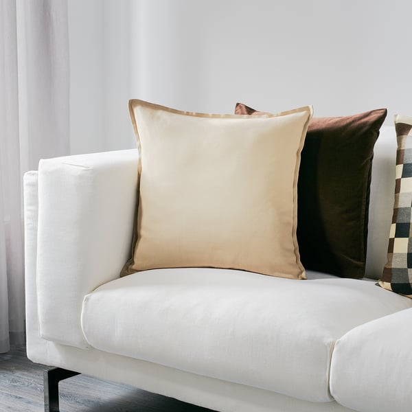 Minimalist living room with white sofa. GURLI pillow is large beige with zipper. Smaller pillows in brown and multicolored patterns.