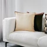Minimalist living room with white sofa. GURLI pillow is large beige with zipper. Smaller pillows in brown and multicolored patterns.