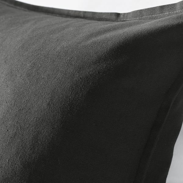 Black cushion cover made of smooth cotton, displayed indoors, illustrating its texture and quality.