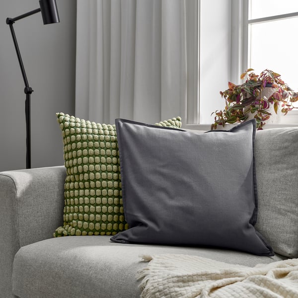Cozy living room with grey pillow, green cushion, lamp, and plant.