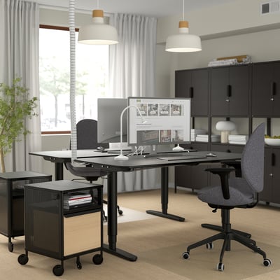 Modern office with black desks, gray chairs, white lights, and storage by large window.