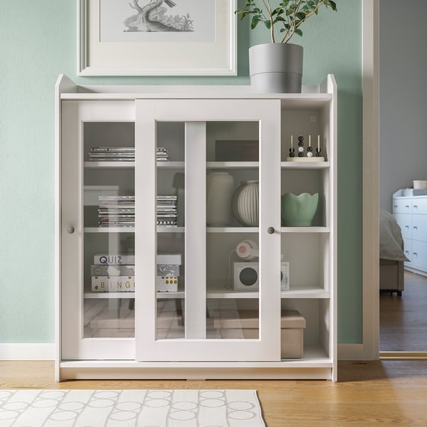 Modern living room with HAUGA white cabinet, glass doors, varied decor items.