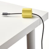 A bright yellow usb anchor neatly holds a black cable on a sleek white desk, showcasing its organizational quality.