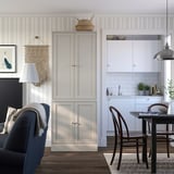 A cozy room with a blue chair, wooden cabinets in natural finish, and a dining table with a hanging lamp.
