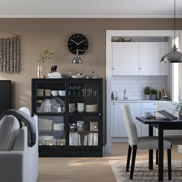 Modern living room with HAVSTA black wooden cabinet, white dishes, gray armchair, white dining set, and wall clock.
