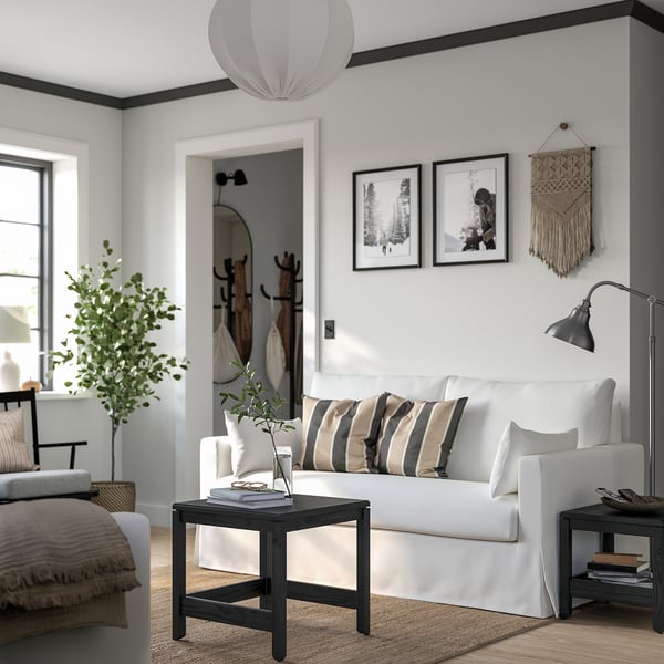 Minimalist living room with white couch, striped pillows, small coffee table, floor lamp, wall art, and indoor plant.