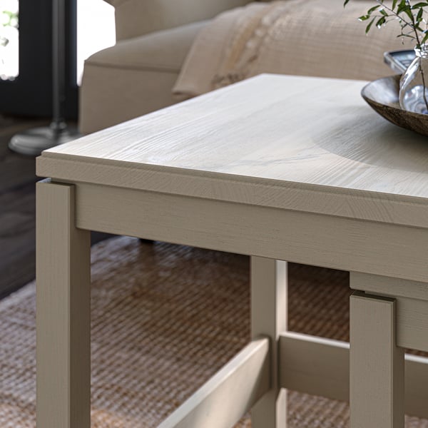 Light wooden nesting tables, light grey finish, simple design, two-tiered with shelf, placed near sofa, minimalist living room.