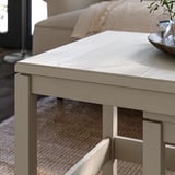 Light wooden nesting tables, light grey finish, simple design, two-tiered with shelf, placed near sofa, minimalist living room.