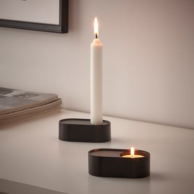 Two modern, rustic black candle holders with lit candles on sleek white table.