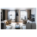 Modern living room with white sofas, glass table, black lamp, shelves with decor, and large windows.