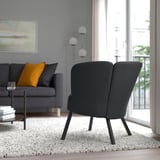 A modern living room with a bold, rounded HERRÅKRA armchair near a window, providing a cozy and comfortable seating space.