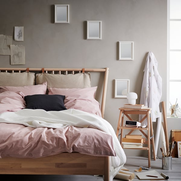 Cozy bedroom with wooden bed, pink pillows, mirrored headboard, side table with lamp, clock, and easel.