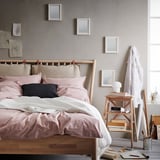 Cozy bedroom with wooden bed, pink pillows, mirrored headboard, side table with lamp, clock, and easel.