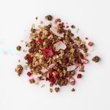 Heaped granola mix with crunchy chocolate oats, coconut flakes, and bright red dried berries on a white surface.