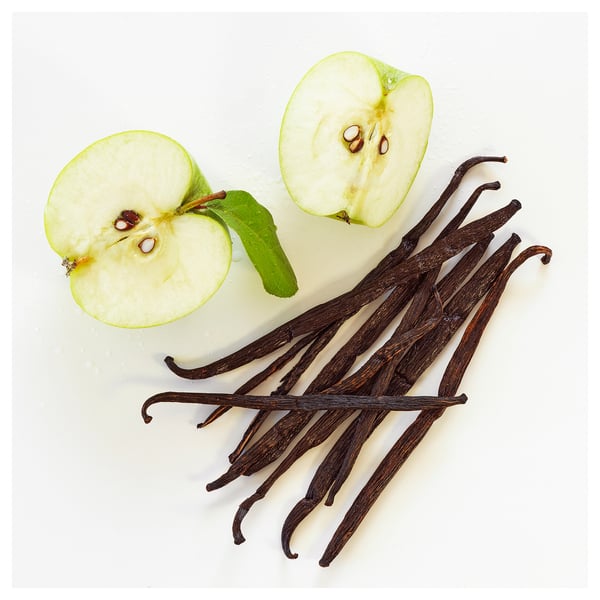 Image shows green apple halves and vanilla pods on white background.