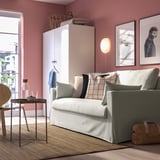 Cozy living room with HYLTARP sofa-bed, neutral pillows, white cabinet, vases, dog photos, and a window.