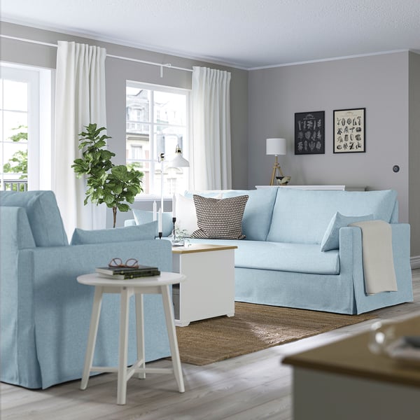 Modern living room with blue sofa, side table, and wall art. Grey walls, light wood floor, and large window.