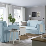Modern living room with blue sofa, side table, and wall art. Grey walls, light wood floor, and large window.