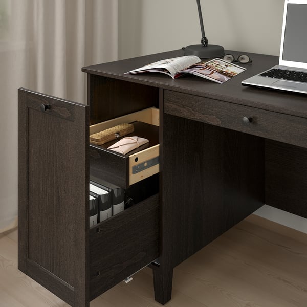Dark wood desk with open drawer revealing neatly stored items. Laptop and magazines on top, showcasing storage and workspace functionality.