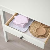 White drawer unit with open drawer revealing pink folded item, woven baskets, and round cork trays. Ideal for organizing personal items.