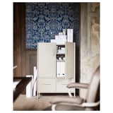 A white IDÅSEN office cabinet with a blue patterned wallpaper backdrop. The cabinet has open drawers and doors revealing storage items.
