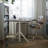 Modern home office with IDÅSEN adjustable desk, gray chair, wooden floor, and large window.