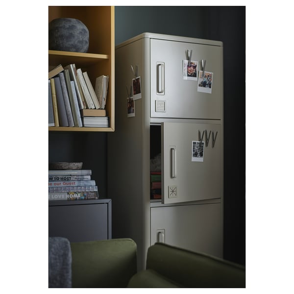 Modern metal storage unit with photos and magnets, beside heavy dark shelves with books.