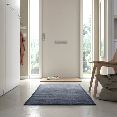 A modern entryway with a blue cotton rug, wooden chair, and red jacket hook.