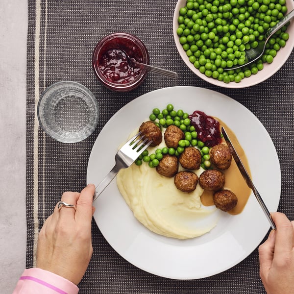 Large plate with meatballs, mash, peas, jam; hands with fork and knife.
