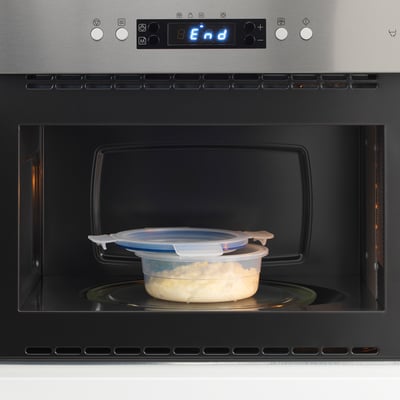 A covered food container sits in a microwave, ready to be heated. The microwaves digital display reads end, indicating the heating cycle is complete.