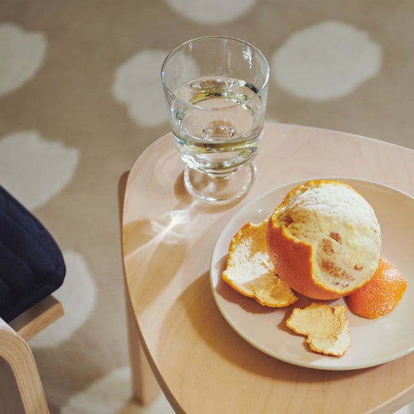 A glass of water sits on a wooden table beside a peeled orange on a plate.