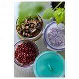 Three glass containers with blue, green, and clear lids hold mushrooms, pomegranate seeds, and sliced red onions, placed on a gray countertop.