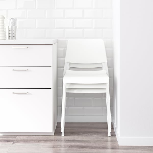 Stackable white ikea chair next to cabinet.