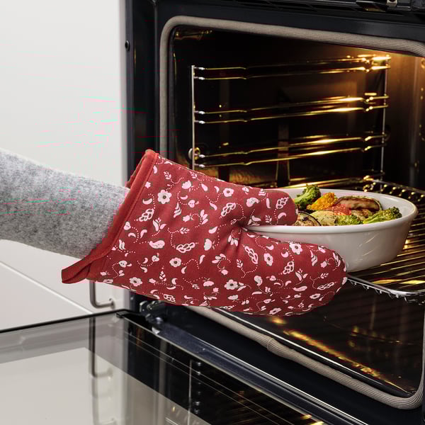 Person placing casserole in oven using red floral-patterned, double-sided oven mitts for protection and easy handling.