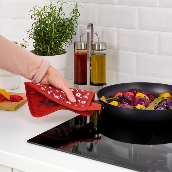 Person cooks colorful vegetables in a skillet using a red mitt to handle the pan.